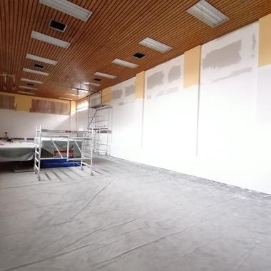 Blick in einen unfertigen Raum mit Gerüst, abgedecktem Boden und frisch verputzten Wänden in unterschiedlichen Farben.