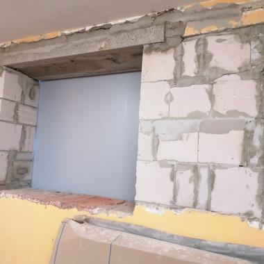 Offenes Fenster in einer Mauer aus weißen Ziegeln, umgeben von frischer Mörtelbeschichtung auf gelbem Putz.