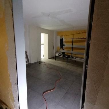 Blick durch einen Türrahmen in einen unvollendeten Raum mit Fliesenboden und gelben Wandregalen.