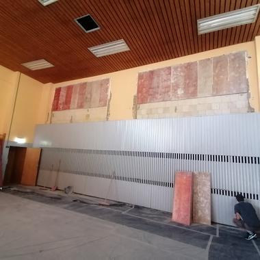 Renovierungsarbeiten in einem Raum mit abblätternder Wandfarbe und einem Arbeiter, der sich um eine graue Wand kümmert.