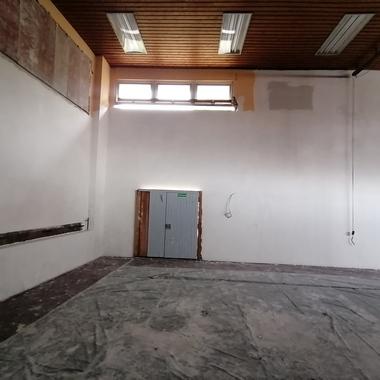 Leere, hell erleuchtete Innenräume mit grauer Wand, Fenster und einer geschlossenen Tür im Hintergrund.