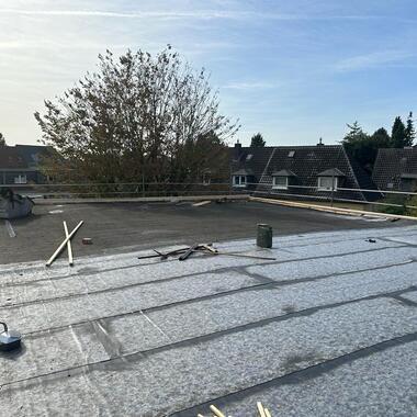 Blick auf ein Flachdach mit Materialien und Werkzeugen, Überdachung und Wohnhäuser im Hintergrund unter klarem Himmel.