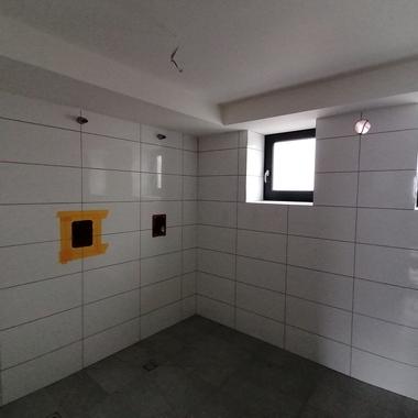 Blick auf einen gefliesten Raum mit zwei Fenstern, Kabeln und Steckdosen in rot mit gelber Umrandung.