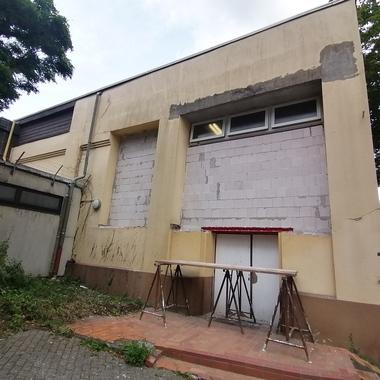 Blick auf eine unvollendete Gebäudefassade mit zwei großen Fensteröffnungen und einer roten Tür unter einem Gerüst.