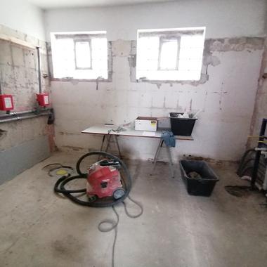 Bauzimmer mit unvollendeten Wänden, einem Staubsauger, einem Tisch und Bauutensilien auf dem Boden.