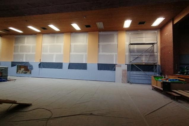 Blick in einen Renovierungsraum mit unvollendeten Wänden, Gerüst und abgedecktem Boden.