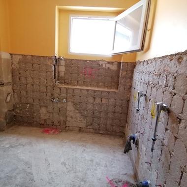 Rohbau eines Badezimmers mit unvollständigen Wänden, offenem Fenster und sichtbaren Wasseranschlüssen.