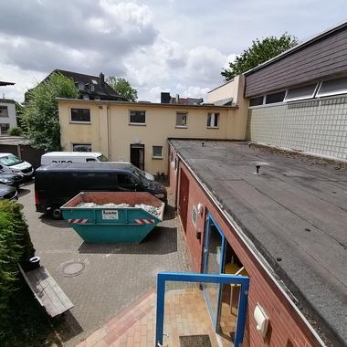 Blick auf einen Innenhof mit mehreren Fahrzeugen, einem Container und angrenzenden Gebäuden im Hintergrund.