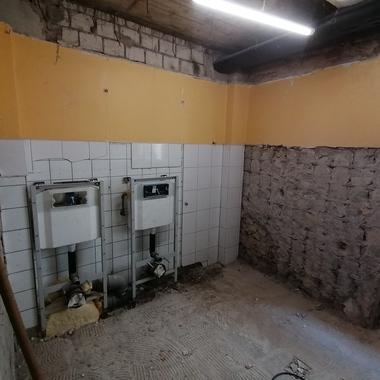 Leere Wand mit zwei installierten Unterputzspülkästen in einem unvollendeten Raum mit unstrukturiertem Boden.