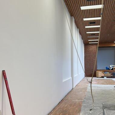 Baustelle mit halbfertig verputzter Wand, Holzboden und abgedecktem Bodenbereich, Decke mit Beleuchtung.