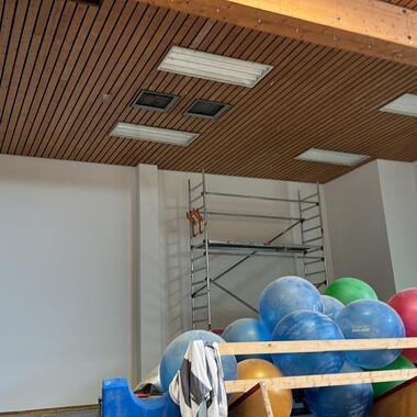Blick in einen Raum mit bunten Gymnastikbällen, einer Holzstiege und Holzdecke; Wände teilweise leer.