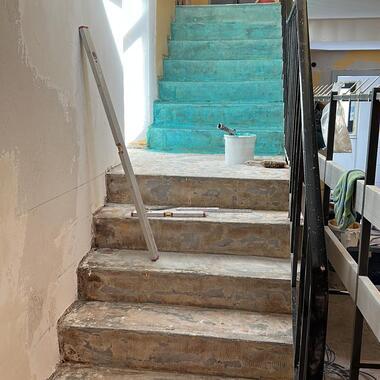 Reparierte Treppe mit grün gestrichenem Geländer und Baugeräten in einem unvollendeten Raum.