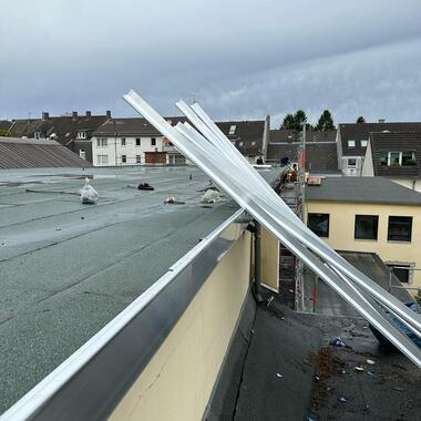 Dachansicht mit weißem Material, das auf der Kante einer grün beschichteten Dachfläche liegt, und grauem Himmel.