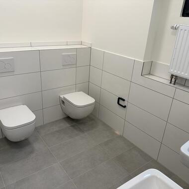 Sauberes, modernes Badezimmer mit zwei hängenden WCs und Waschbecken auf grauem Fliesenboden.