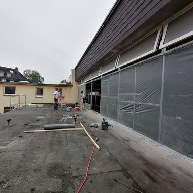 Arbeiter auf einem Flachdach mit Gerüst, Werkzeugen und Materialien zur Renovierung eines Gebäudes im Hintergrund.