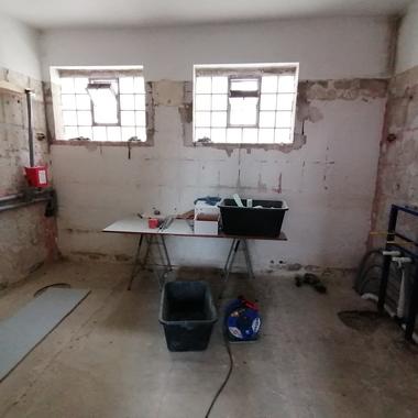 Leere, unrenovierte Innenräume mit zwei Fenstern, einem Tisch, Werkzeugen und Rohrleitungen an den Wänden.