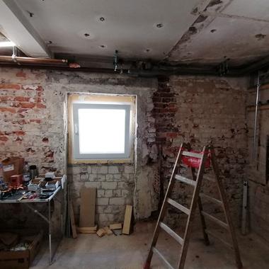 Renovierungsraum mit Mauerwerk, Fenster, Leiter und einem Tisch voller Werkzeug und Materialien.