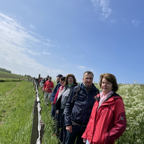 Gruppe von Wanderern steht entlang eines Weidezauns auf einem grünen Feld unter blauem Himmel.