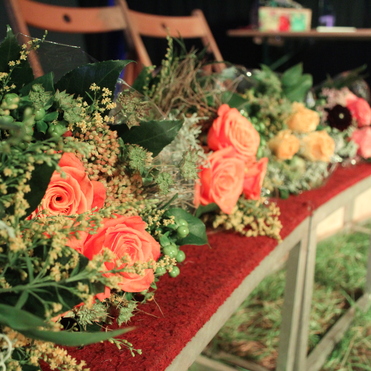 Bunte Blumenarrangements mit orangen Rosen und grünen Blättern auf einer roten Struktur im Vordergrund.