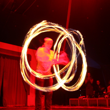 Feuerspucker führt beeindruckende Künste mit brennenden Fackeln in einem Zirkuszelt auf, Publikum im Hintergrund.