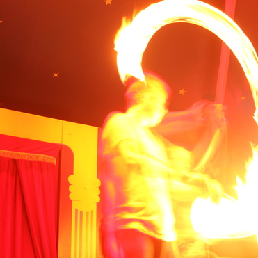 Flammenschwingen eines Artisten in einem Zelt mit rotem und gelbem Hintergrund. Bewegung erzeugt eine dynamische Lichtspur.