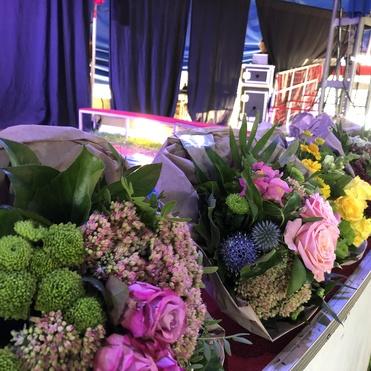 Reihe von bunten Blumensträußen auf einem Tisch, im Hintergrund eine Zeltatmosphäre mit schwarzen Vorhängen.