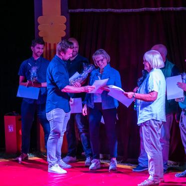 Gruppe von fünf Personen auf einer Bühne, die Urkunden und Geschenke bei einer Zeremonie überreichen.