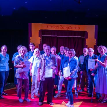 Gruppe von Menschen mit Urkunden und Blumen im Zirkuszelt von Circus Zapp/Zarap auf rotem Teppich.