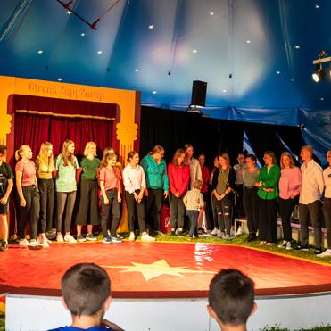 Gruppe von Jugendlichen und Erwachsenen steht auf einer Zirkusbühne mit rotem Boden im Circus ZappZarap.
