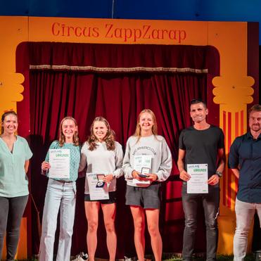 Sechs Personen stehen vor einem roten Vorhang im Circus ZappZarap, halten Urkunden und lächeln.