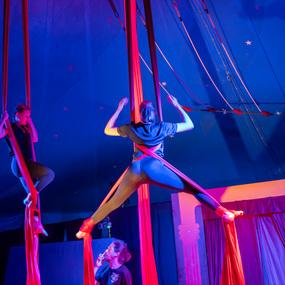 Zwei Artistinnen hängen an roten Tuchbändern in einer Zirkusmanege mit blauer Beleuchtung.
