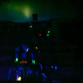 Gruppierte Personen in dunklem Raum mit leuchtenden Armbändern und Accessoires, umgeben von schwacher Beleuchtung.