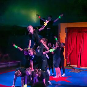 Gruppe von Akrobaten führt eine Pyramide auf einer bunten Bühnenfläche in einem Zirkuszelt auf.