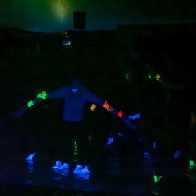 Gruppentanzaufführung im Dunkeln mit neonfarbenen Handschuhen und Schuhen, beleuchtet von Schwarzlicht.