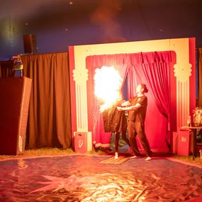 Zwei Künstler führen eine Feuershow in einem Zelt auf, während Flammen aus einem der Kostüme schlagen.