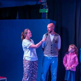 Frau interviewt einen Mann im Zelt, während ein Mädchen in rosa Jacke aufmerksam zuschaut.