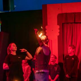 Feuerspucker in einem Zirkus auf der Bühne, umgeben von staunenden Zuschauern in einem roten Licht.