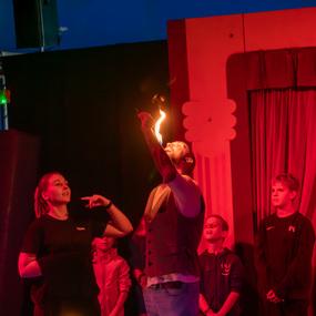 Zirkusvorstellung mit einem Feuerakrobaten, der eine Flamme im Mund hält, umgeben von staunenden Zuschauern.