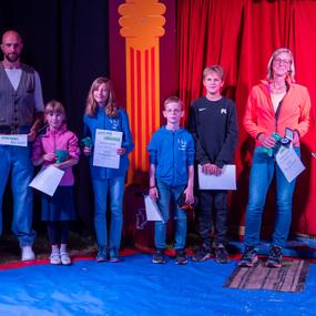 Gruppe von sechs Personen auf einer Bühne, die Urkunden und Preise in den Händen halten, vor rotem Vorhang.