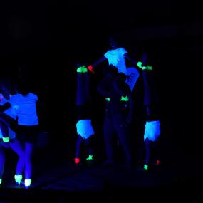 Gruppendynamik von Kindern in leuchtenden T-Shirts und Armbändern im Dunkeln, einige machen Handstände.