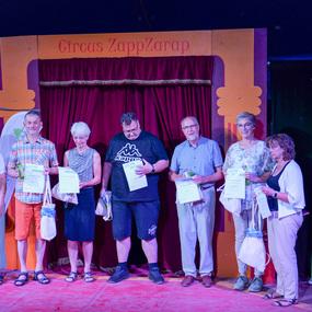 Gruppenfoto von sechs Personen mit Urkunden und kleinen Geschenken auf der Bühne des Circus ZappZarap.