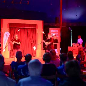 Zwei Artisten führen in einem Zelt eine Feuerjonglage vor, während das Publikum gespannt zuschaut.