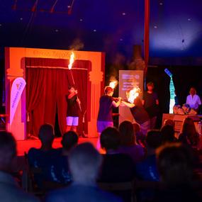 Zwei Künstler führen im Zelt des Cirque ZappZapp eine Feuershow vor einem Publikum auf.