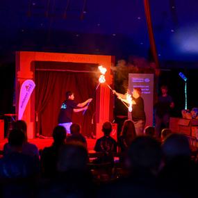 Zwei Artisten führen im Zirkuszelt eine Feuershow auf, während das Publikum gebannt zuschaut.