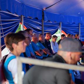 Gruppe von Menschen sitzt in einem Zelt, fokussiert auf eine Präsentation, umgeben von blauen Vorhängen.