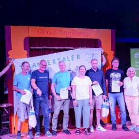 Gruppenszenen mit sieben Personen auf der Bühne des Circus ZappZarap, präsentiert Urkunden vor einem Banner.