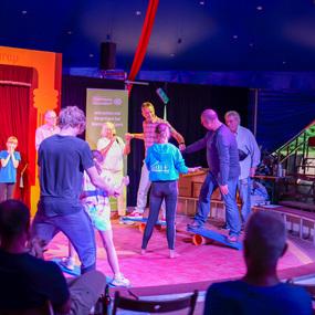 Gruppendarbietung im Zirkus mit Kindern und Erwachsenen auf Balancetools unter einer bunten Zeltkuppel.