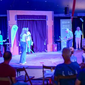 Auf der Bühne des Zirkus ZappZarap führen Künstler eine Darbietung vor einem Publikum in Stühlen auf.