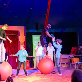 Circusaufführung mit Akrobaten auf großen Bällen, die balancieren und miteinander interagieren. Zuschauer beobachten gespannt.