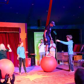 Zwei Artisten performen im Zirkus ZappZarap auf großen Bällen, während das Publikum zusieht und applaudiert.